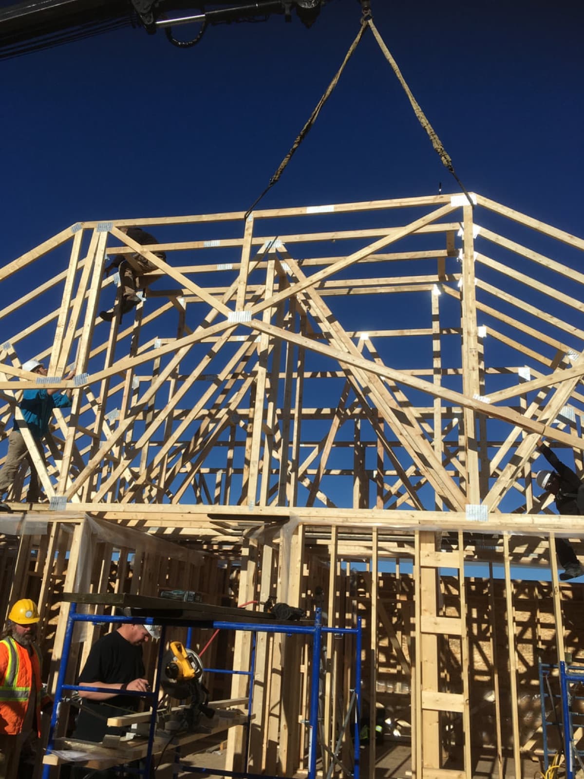 A complete roof truss system being craned into place against a clear blue sky